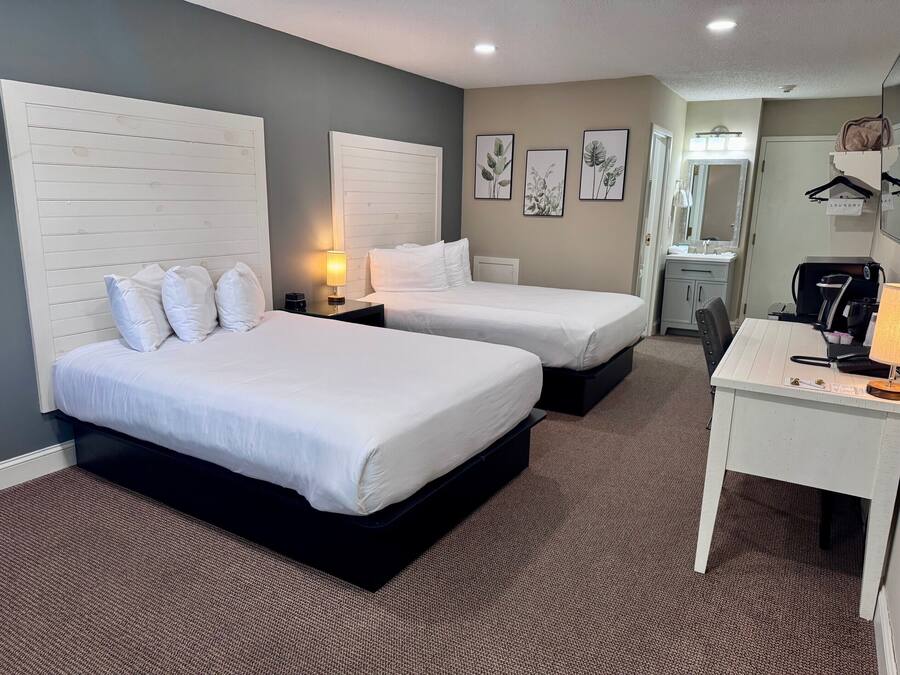 Quarto de hotel com duas camas, uma escrivaninha, um espelho e uma pequena cozinha.