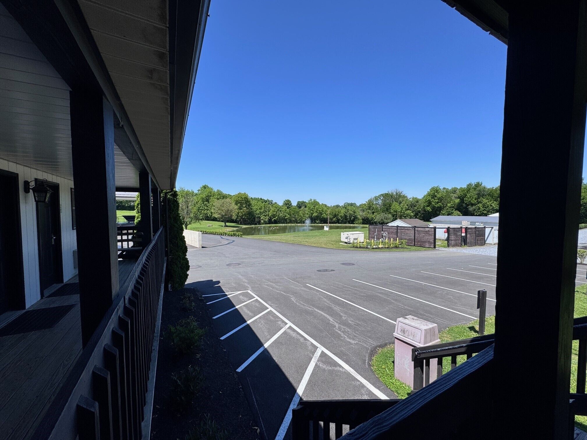 A view from a balcony overlooking a parking lot with a building in the foreground and a lake in the background.