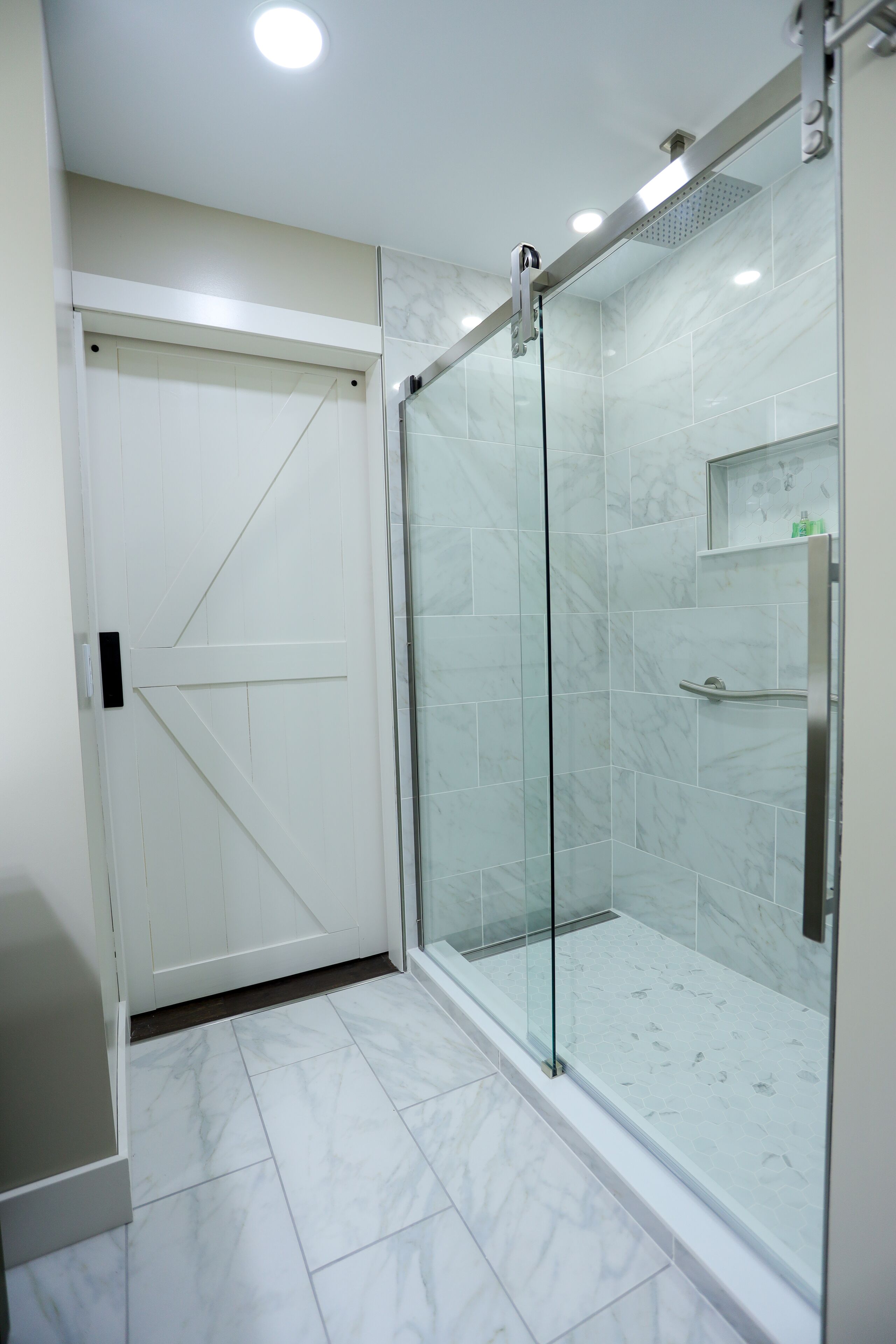 Une salle de bain moderne avec une douche à parois de verre, des murs recouverts de carreaux blancs et une porte blanche.