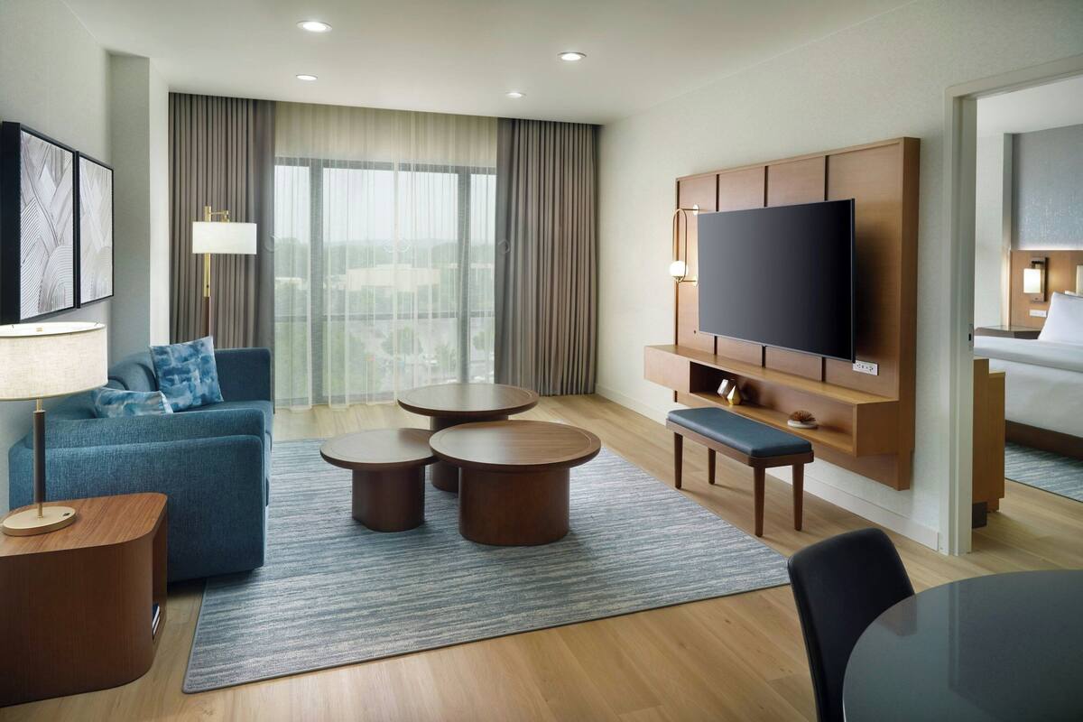 Een moderne hotelkamer met een grote flatscreen-televisie, een bank, twee ronde salontafels, een leuning en een eettafel.