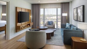 Una habitación de hotel moderna con un televisor de pantalla plana grande, un sofá, una mesita redonda y una pequeña mesita auxiliar.