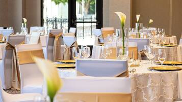 A banquet hall with tables set for a formal event, featuring white tablecloths, gold chargers, and floral centerpieces.