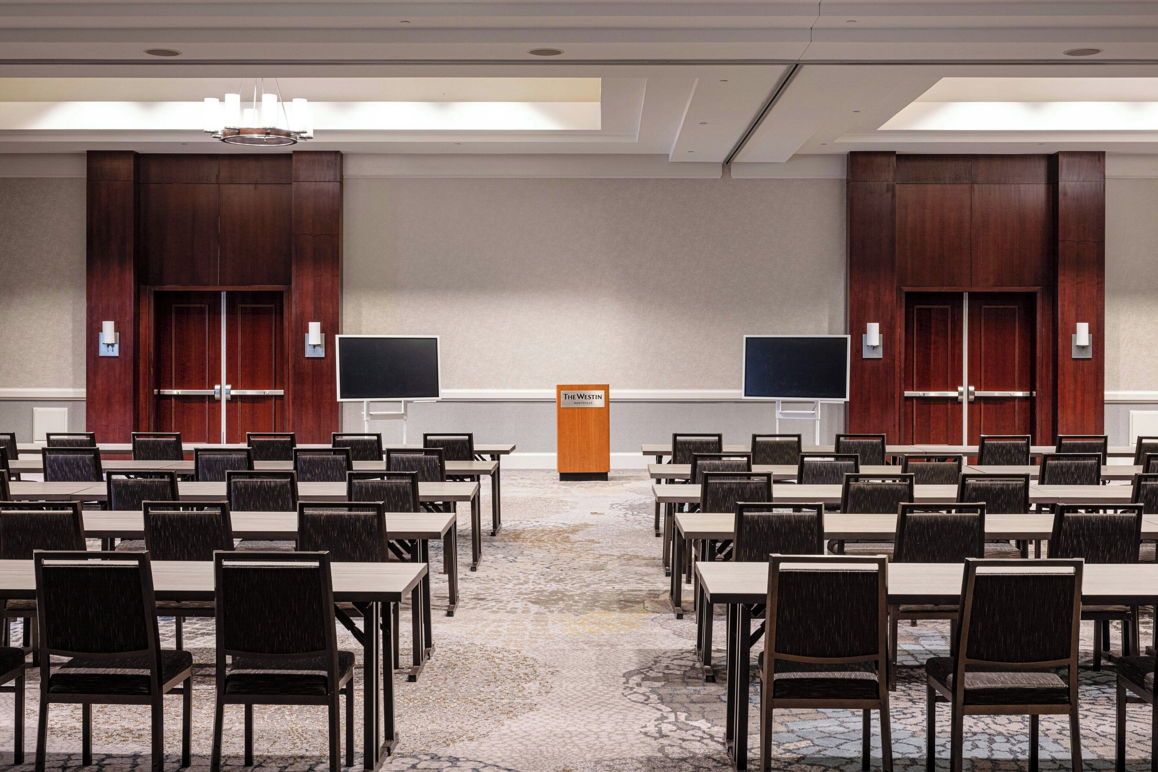 A conference room with multiple tables and chairs, two large screens, and a podium labeled "The Westin".