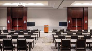 A conference room with multiple tables and chairs, two large screens, and a podium labeled "The Westin".