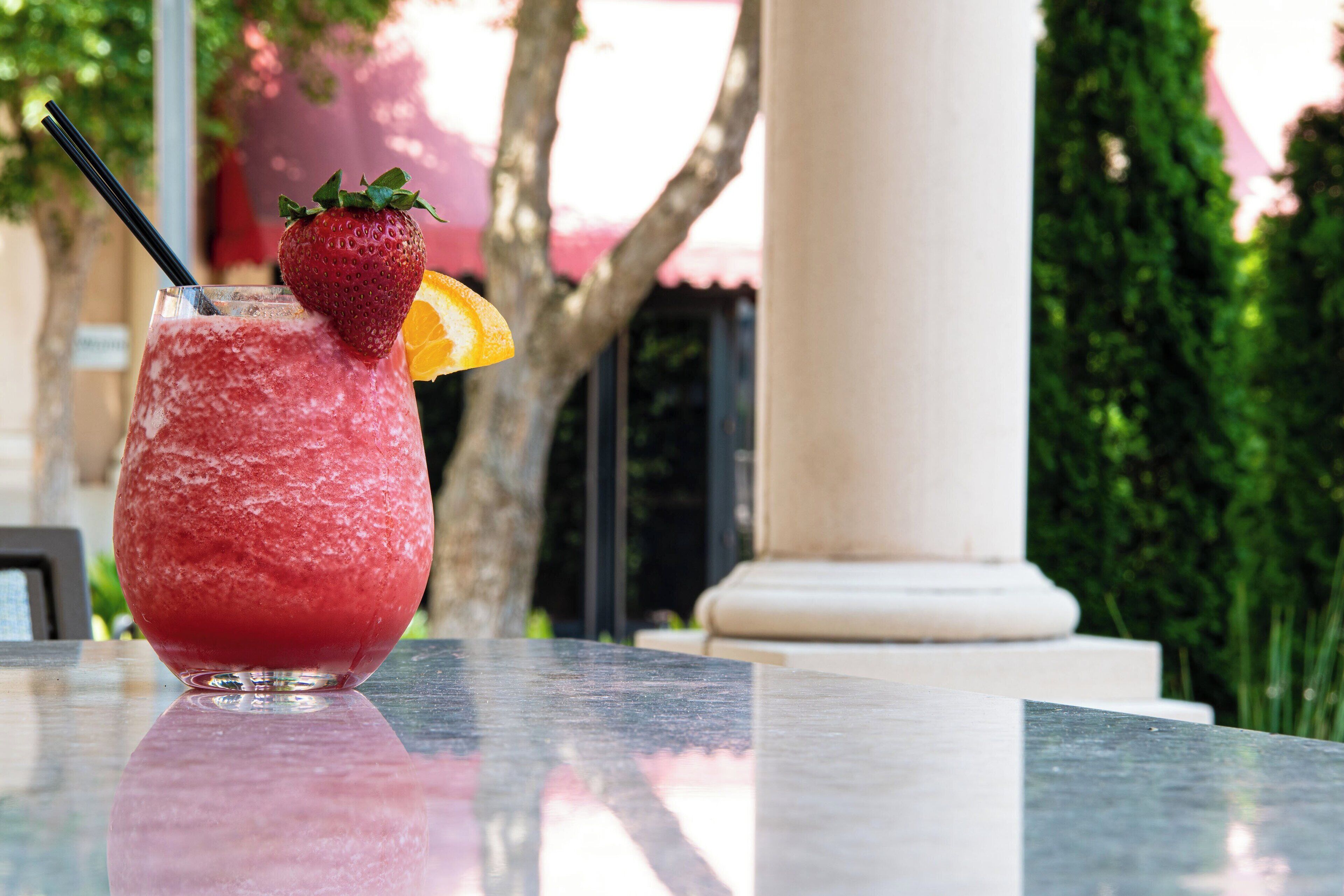 A glass of red beverage with a strawberry and orange slice garnish on a marble table outdoors.