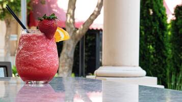 A glass of red beverage with a strawberry and orange slice garnish on a marble table outdoors.