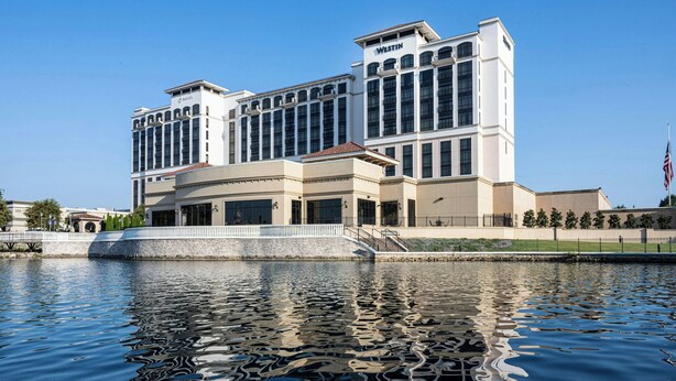 Un hotel grande y moderno con un llamativo letrero de Westin, reflejado en agua tranquila.