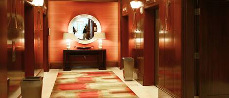 A hotel hallway with a red carpet, a round mirror above a console table, and wooden walls.