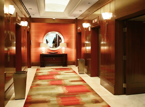 Un pasillo de hotel con alfombra roja, un espejo redondo sobre una consola y paredes de madera.