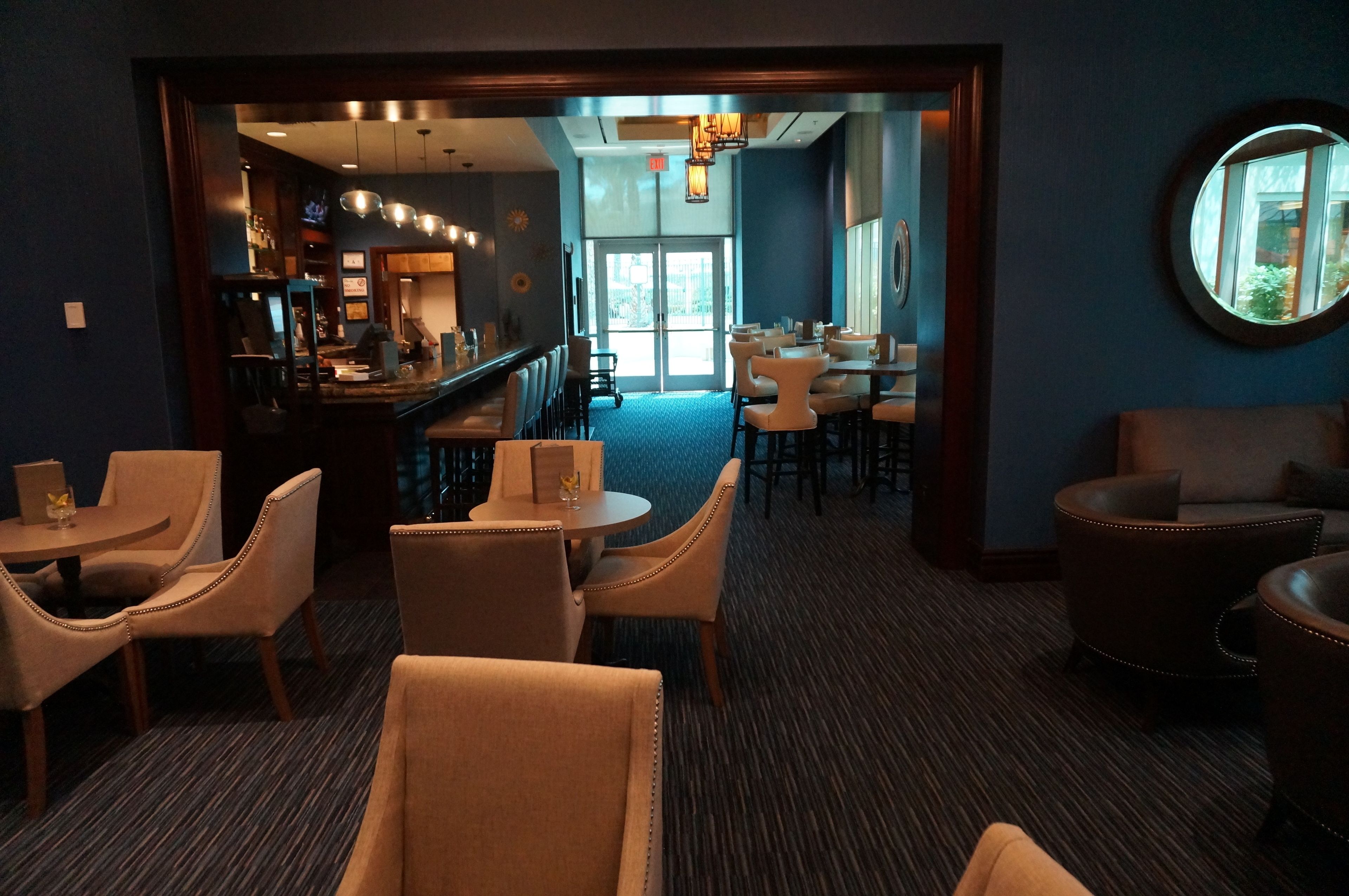 A hotel lobby with a bar area, seating arrangements, and a view of the outdoors.