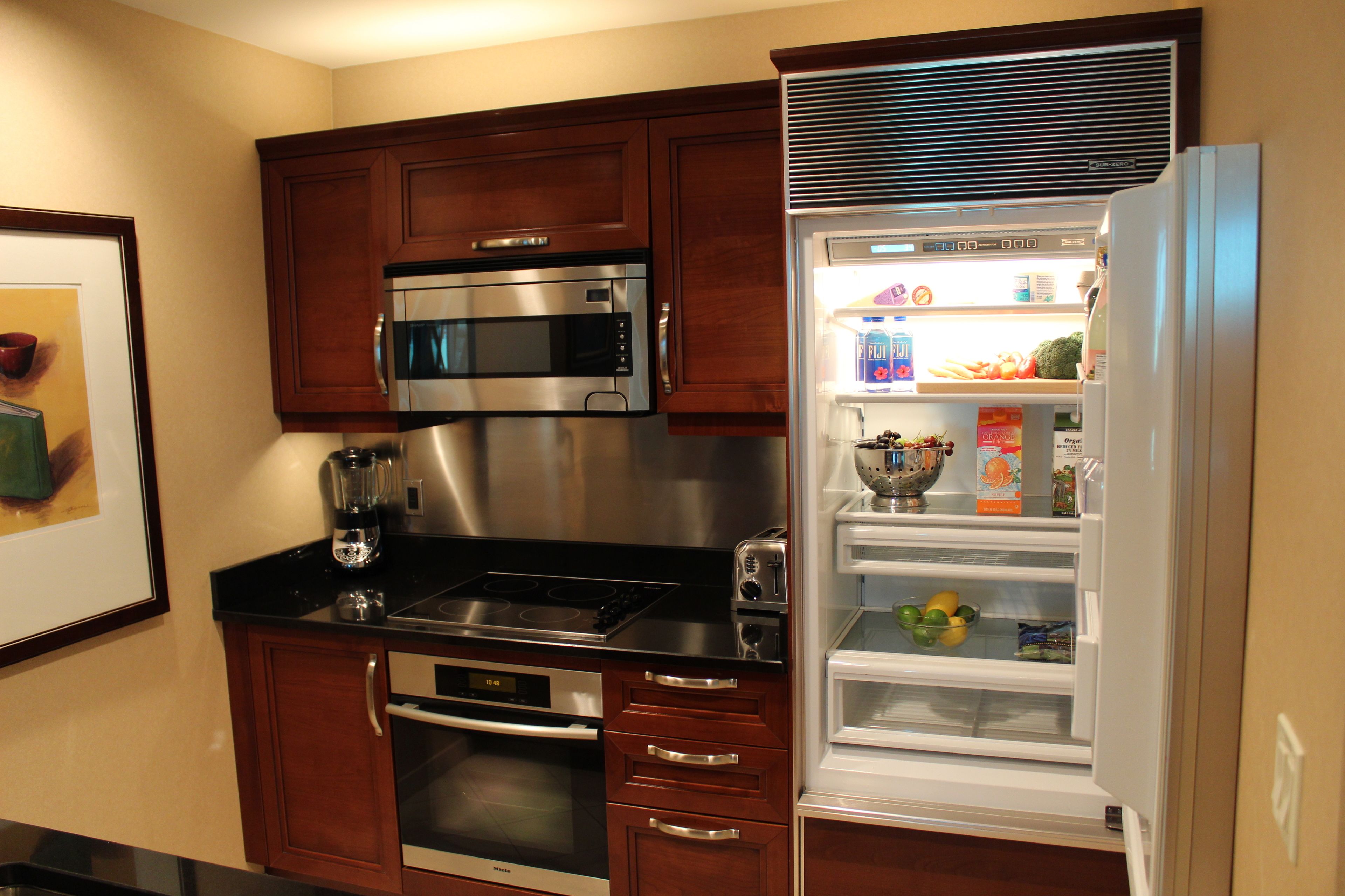 A kitchen with wooden cabinets, a stainless steel microwave, a built-in oven, a toaster, and a white refrigerator with a freezer.