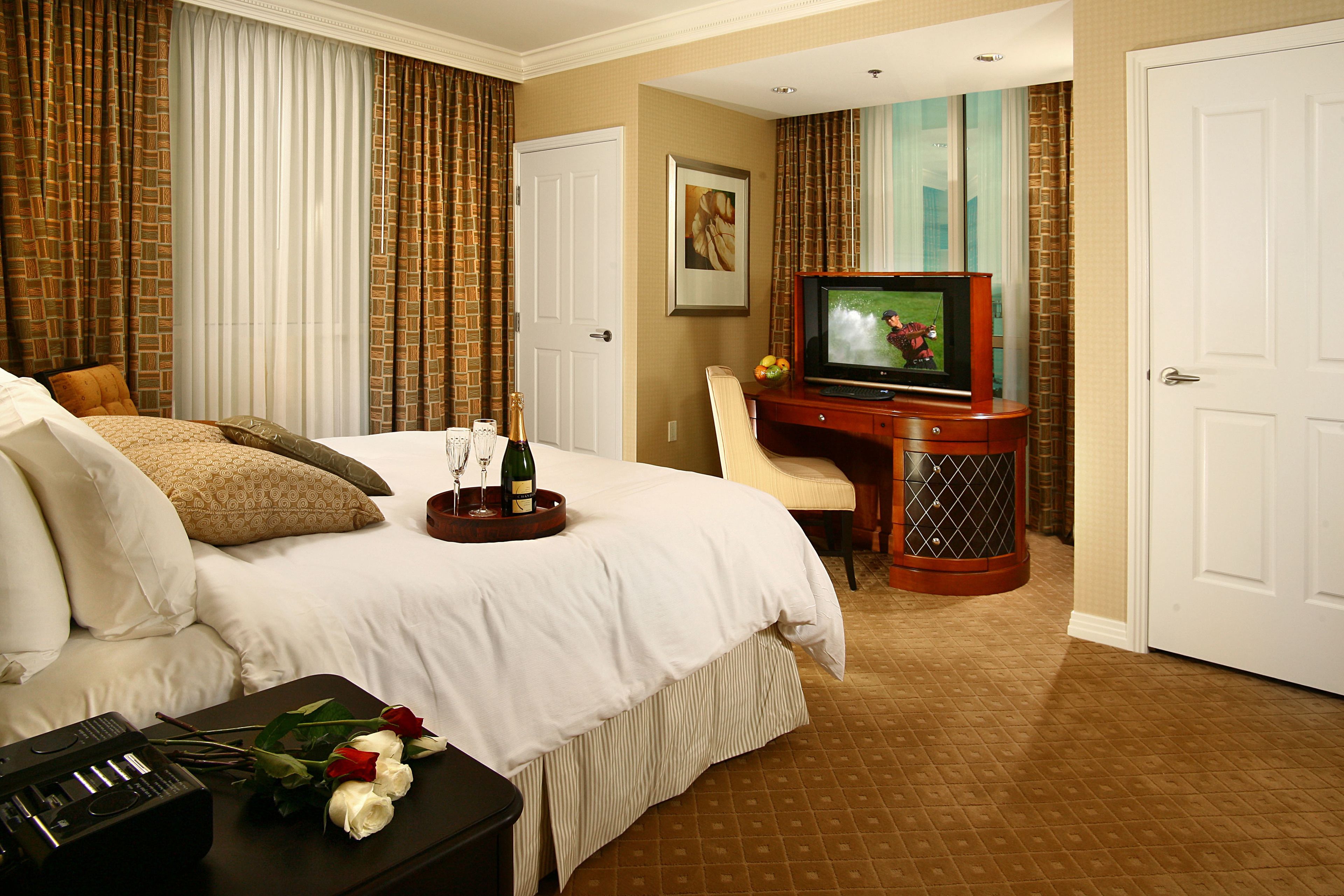 Quarto de hotel com cama, escrivaninha, televisão, minibar e um arranjo de flores.