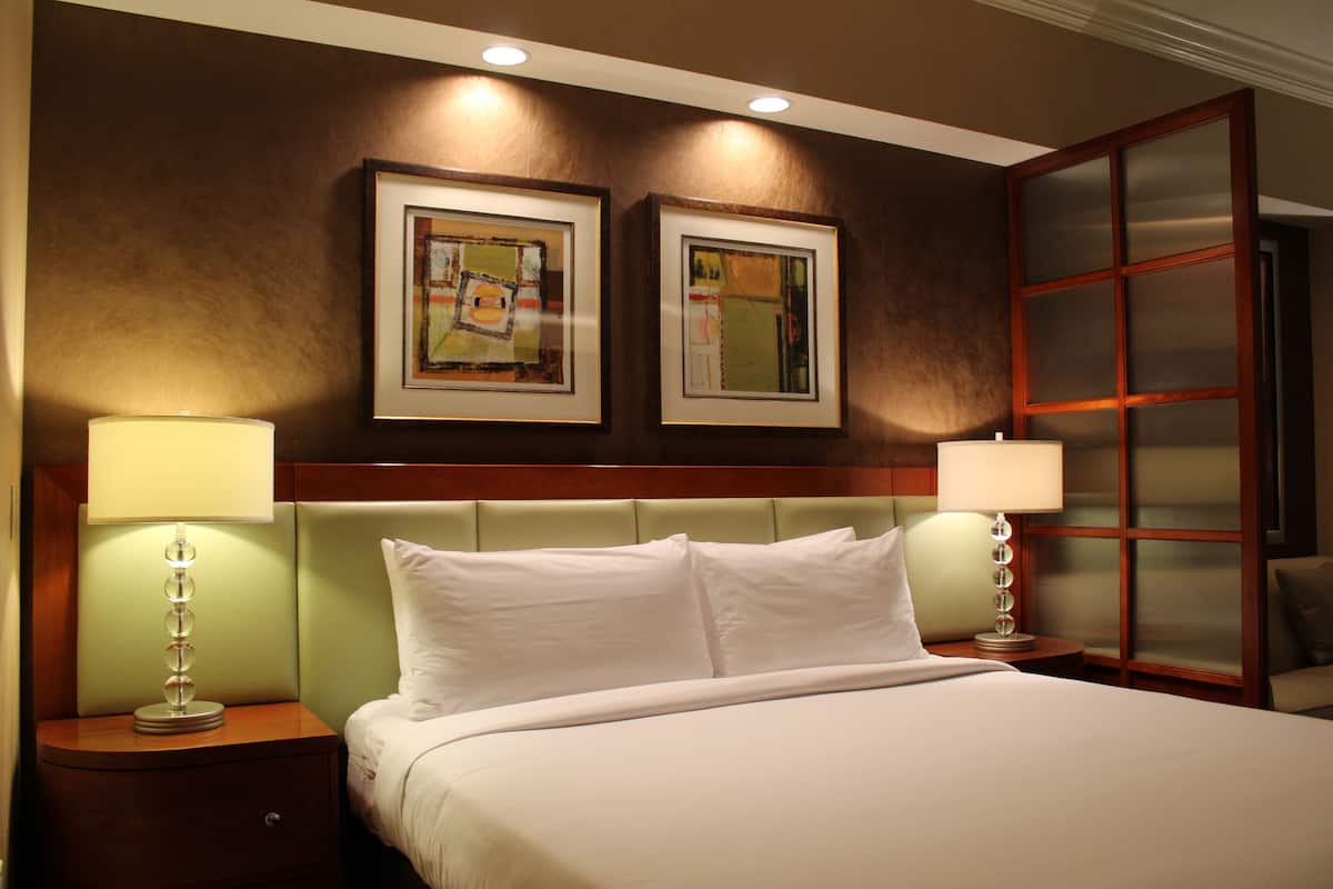 Una habitación de hotel con una cama grande, dos mesitas de noche con lámparas, un cabecero y dos obras de arte enmarcadas en la pared.