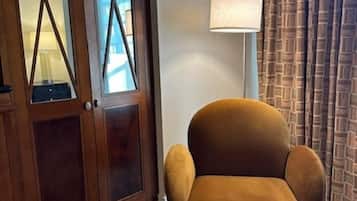 A room with a wooden wardrobe, a brown armchair, a floor lamp, and a patterned curtain.