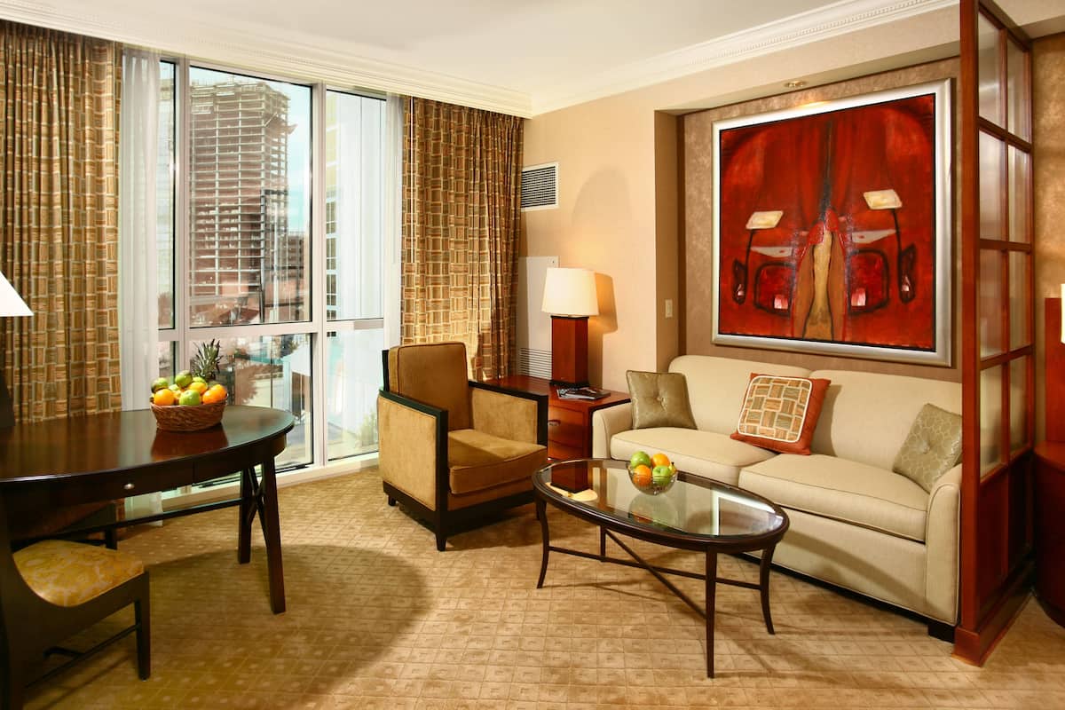 Habitación de hotel con una mesa de comedor, un sofá, una mesa de centro y un ventanal con vistas a la ciudad.