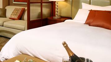 A hotel room with a bed, a nightstand, a lamp, a framed picture on the wall, and a tray with a bottle of champagne and two glasses.