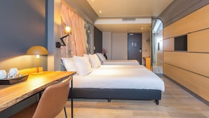 Quarto de hotel moderno com uma cama grande, uma escrivaninha com abajur e vista para o corredor.