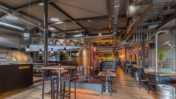 Restaurante moderno com canos aparentes e um espaço de bar.