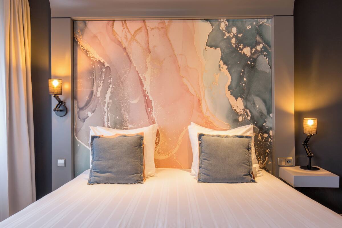A modern hotel room with a large bed, two bedside lamps, and a marble wall mural.