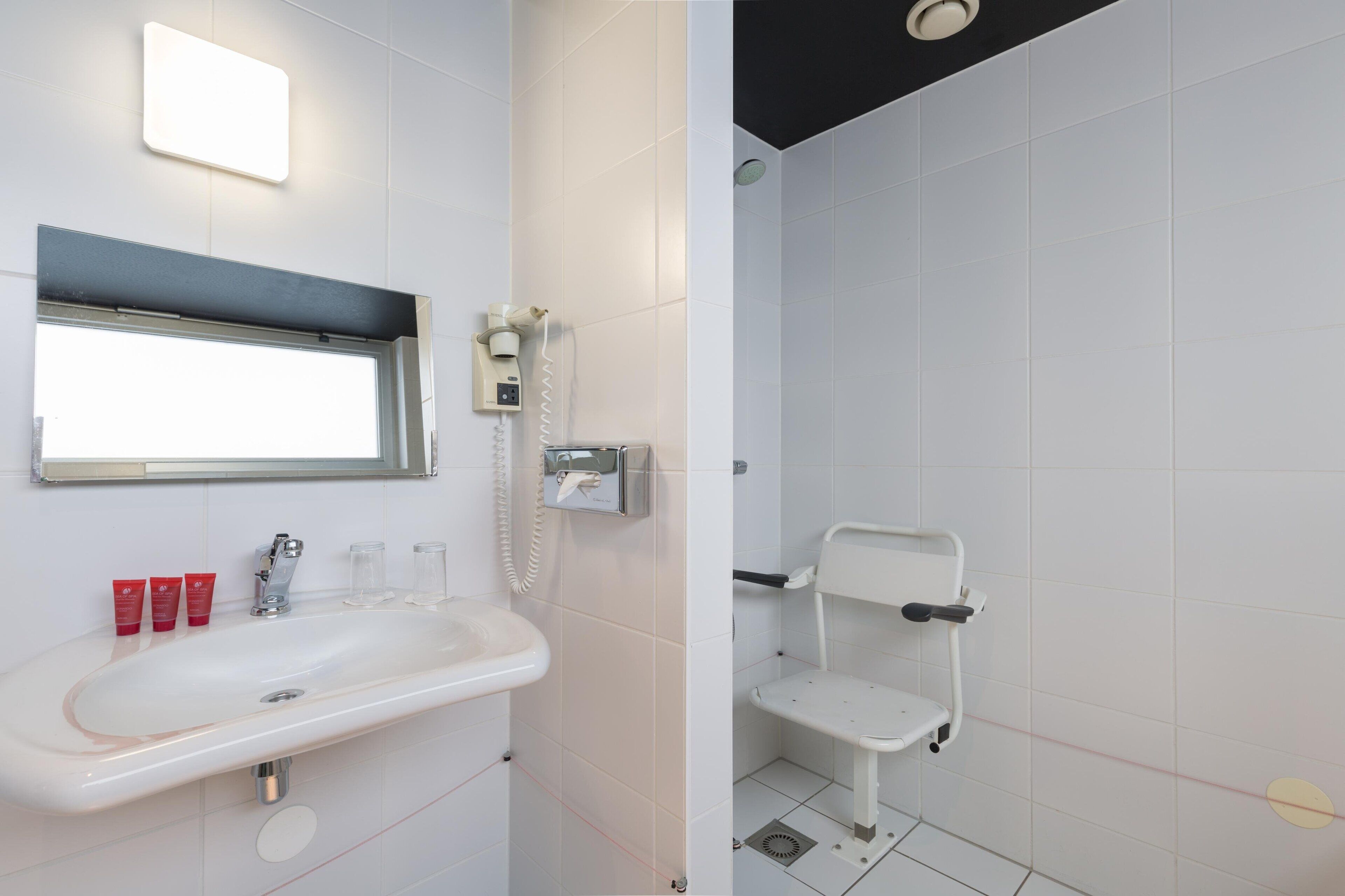 Une salle de bain équipée d’un lavabo, d’un miroir et d’un espace douche avec un siège.