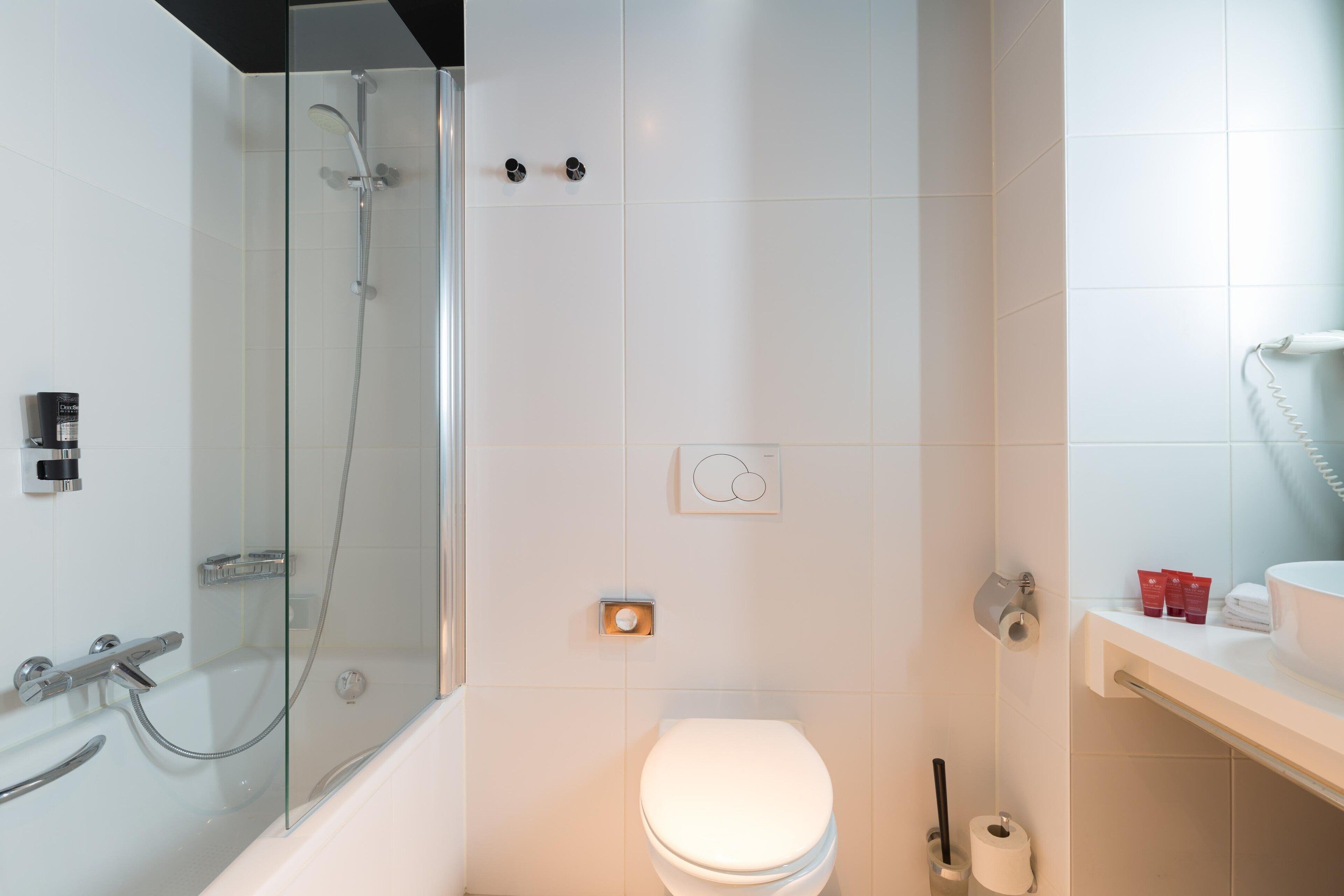 A modern bathroom with a glass-enclosed shower, a white toilet, and a sink with toiletries.