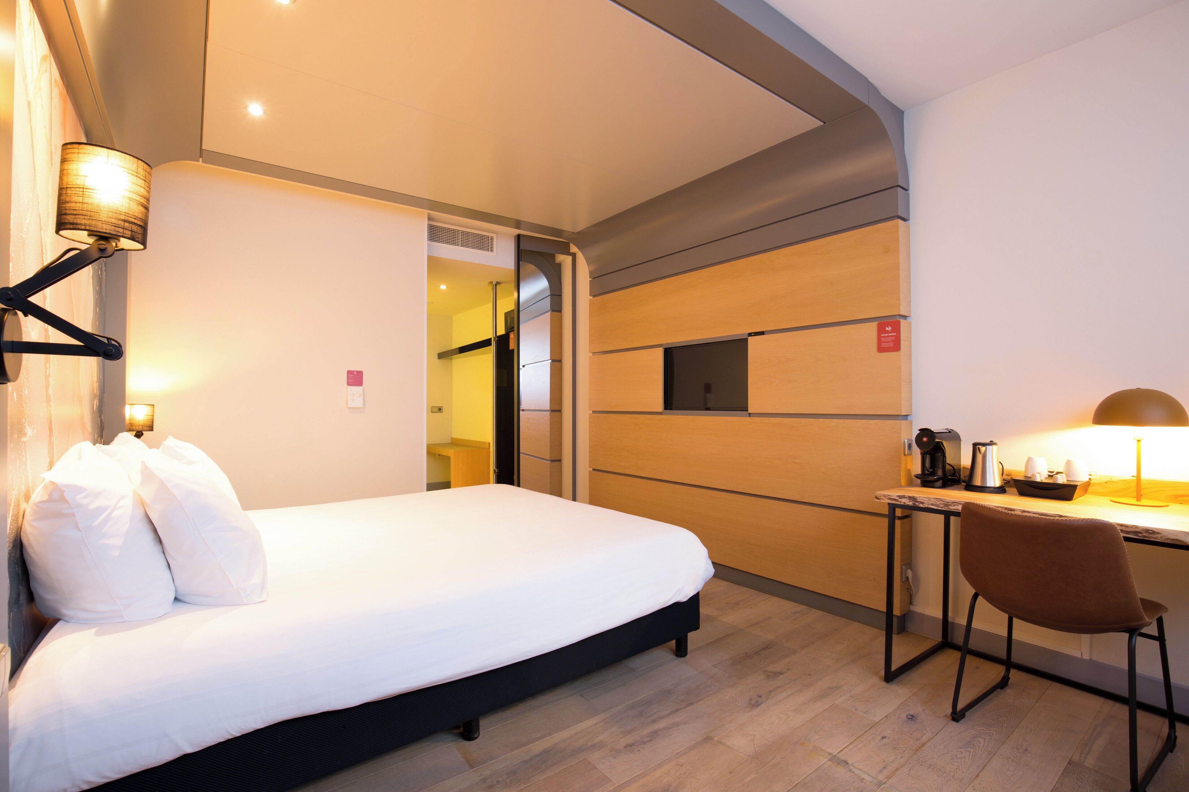 Una habitación de hotel con cama, escritorio, silla y lámpara.