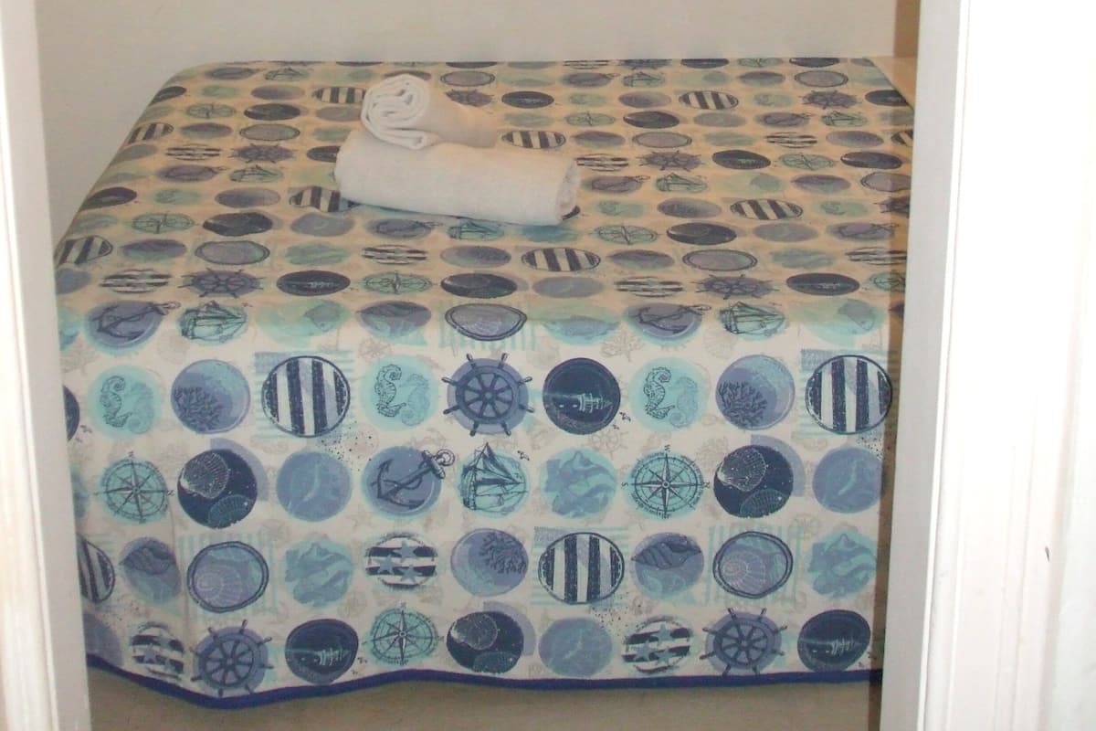 Una habitación pequeña con cama individual, colcha estampada y una toalla enrollada sobre la cama.