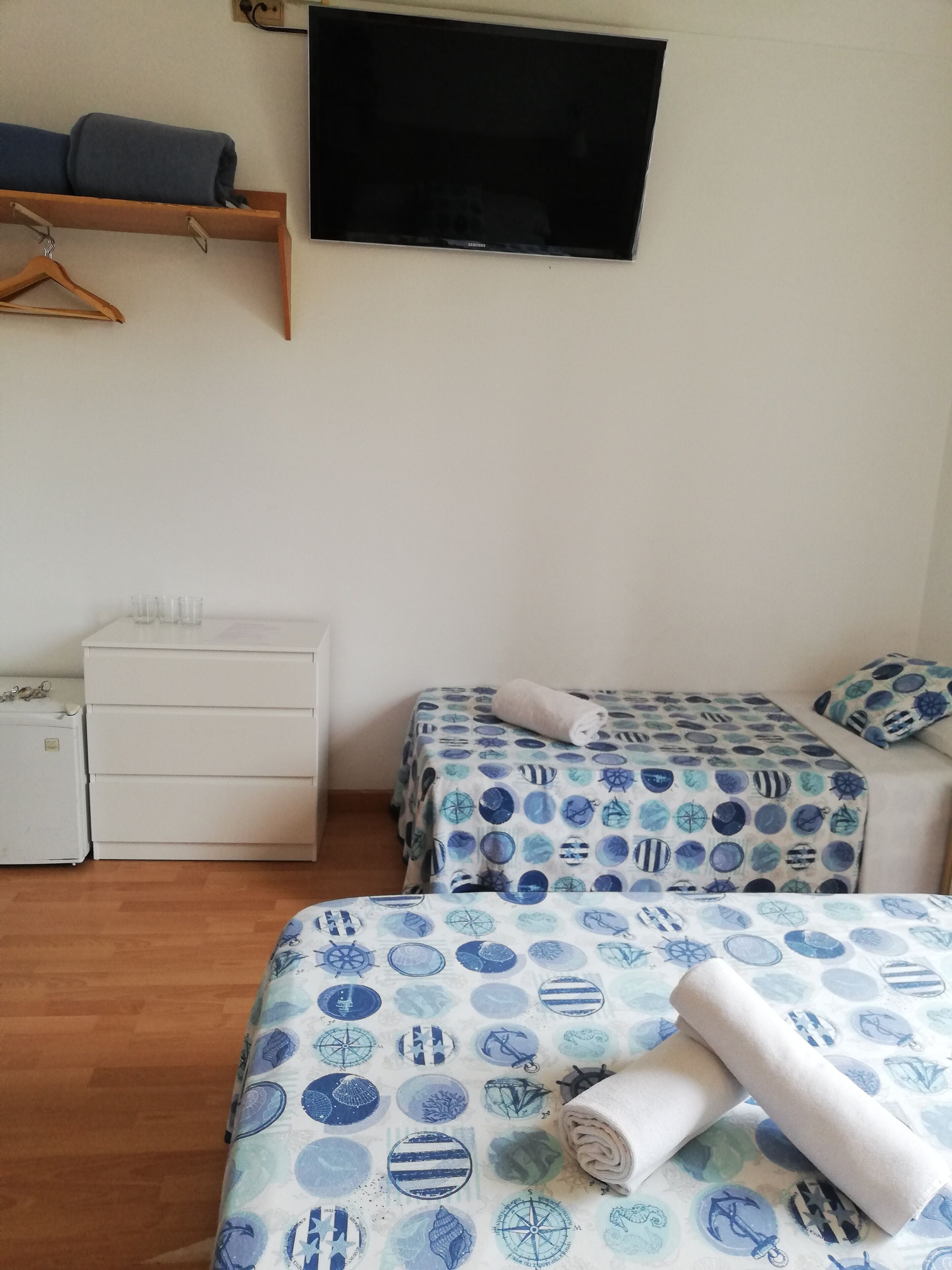 A bedroom with two beds, a TV, a dresser, and a small fridge.