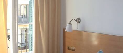 A hotel room with a bed, a nightstand, a lamp, and a view of the outside balcony.