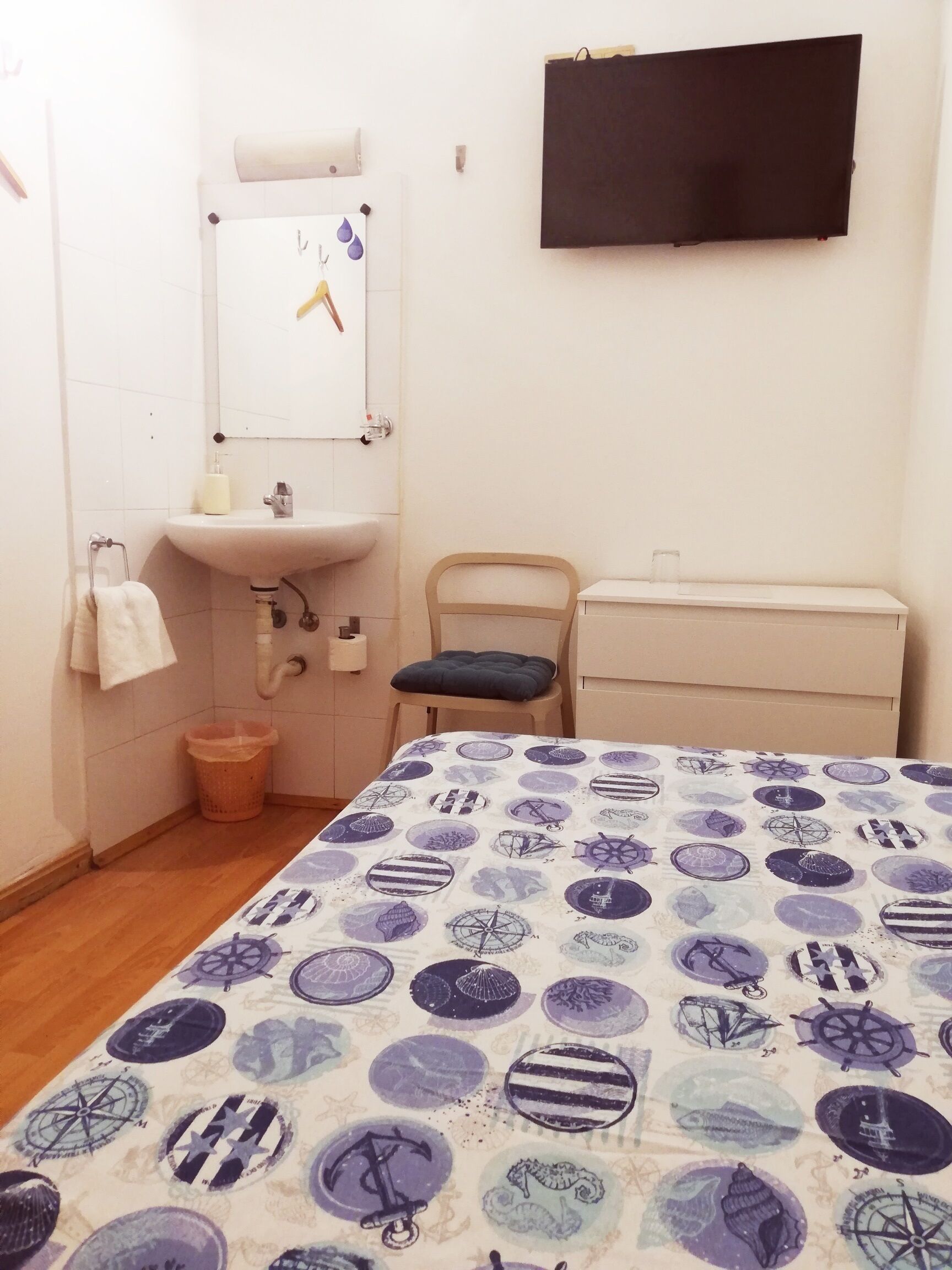 Une petite pièce propre, avec un lit, une chaise, un lavabo et un miroir.