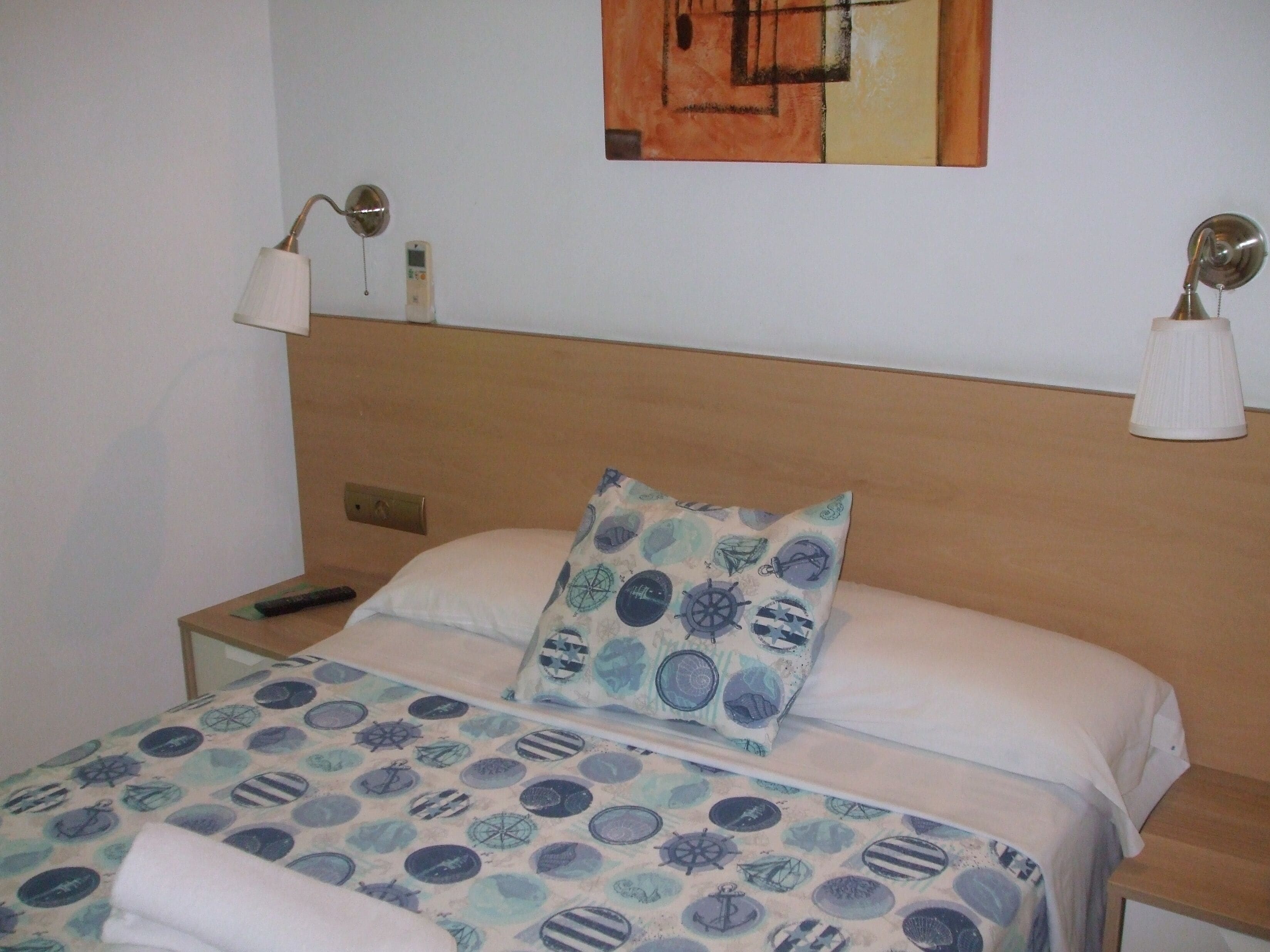 Un lit bien fait, recouvert d’une couvre-lit à motifs, avec un oreiller orné de motifs marins et deux lampes de chevet.
