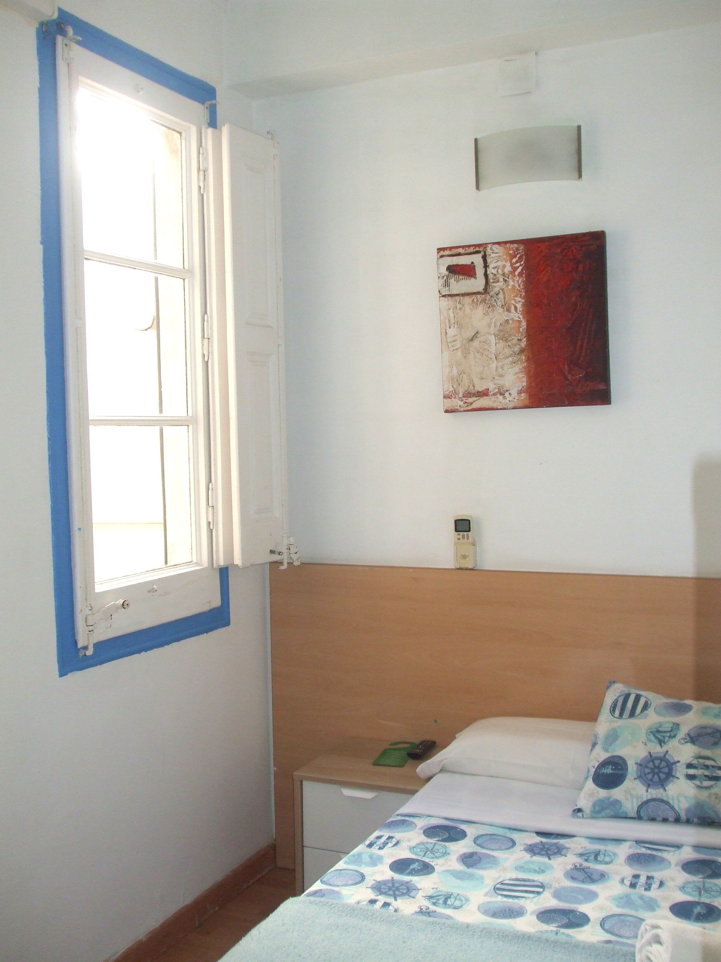 Un dormitorio con cama, mesita de noche, calentador en la pared y ventana con detalles azules.