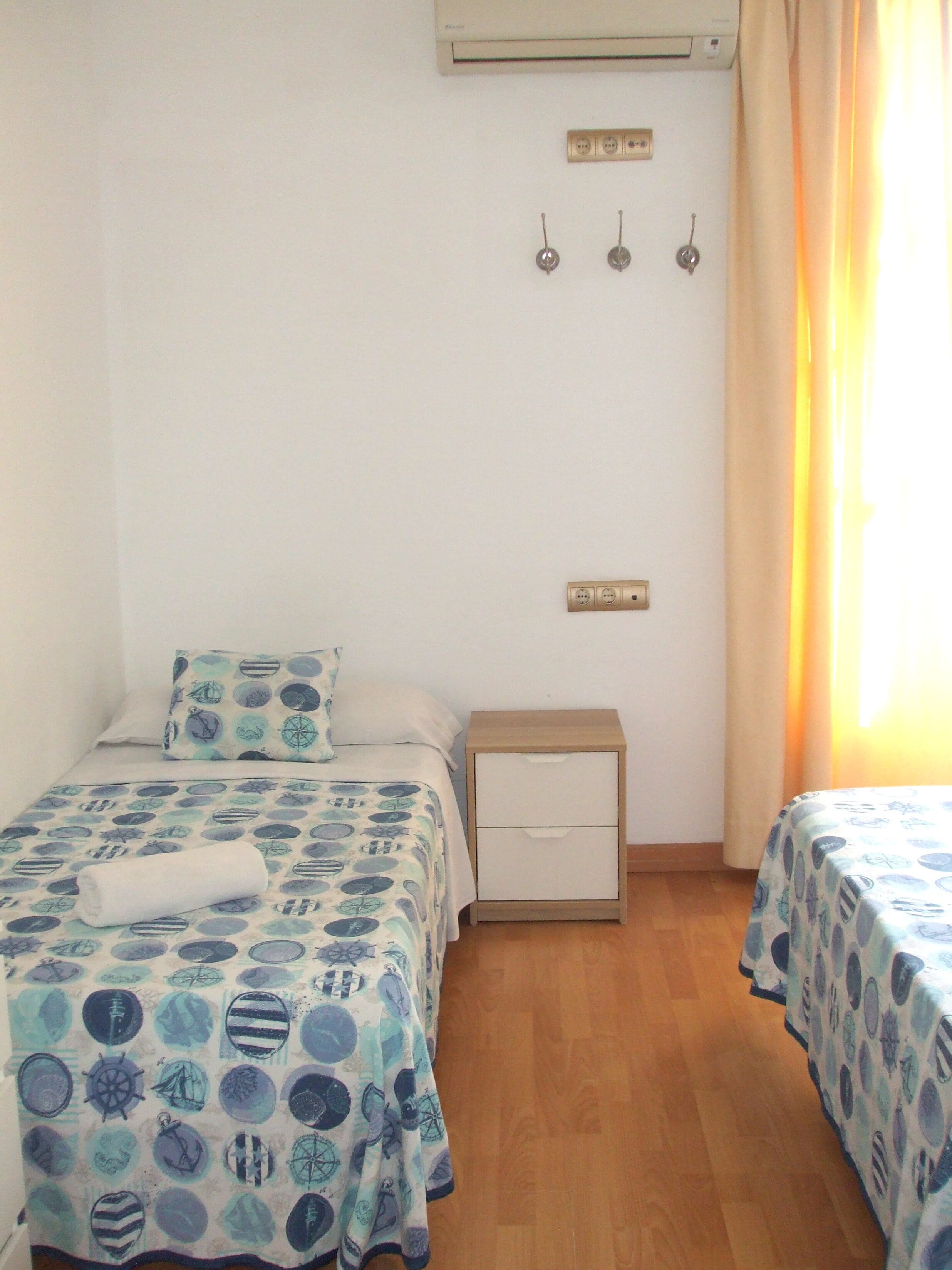 A bedroom with two beds, a nightstand, an air conditioning unit, and a power outlet.