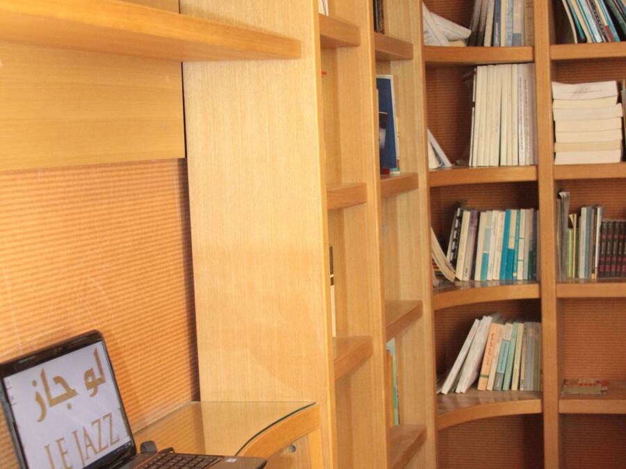 Una biblioteca con estanterías, un ordenador portátil sobre una mesa y una silla.