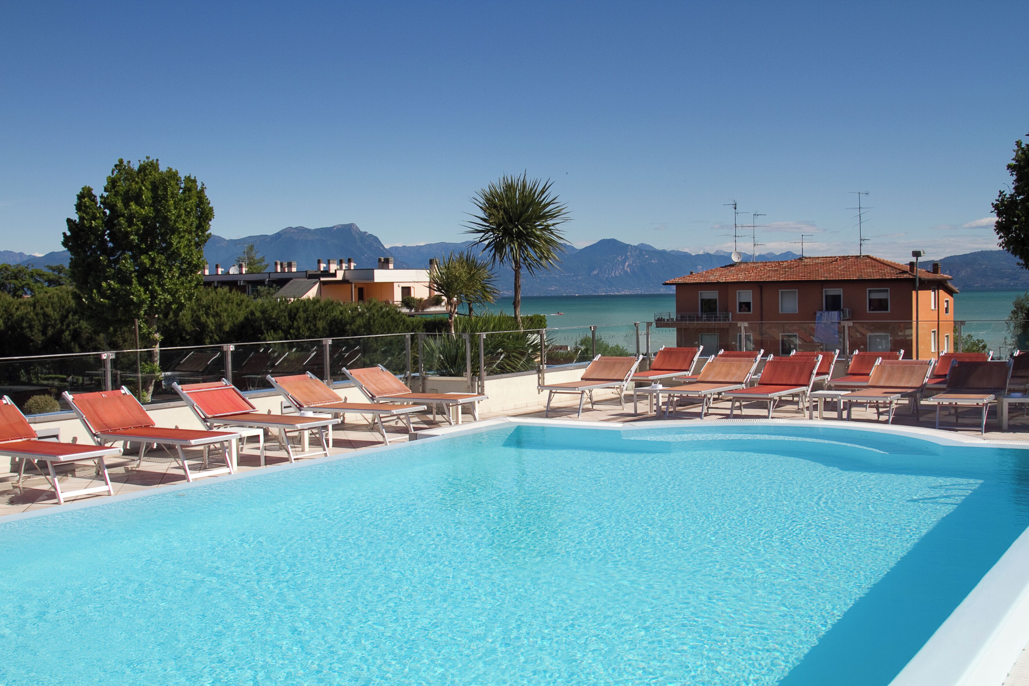 A swimming pool with sun loungers and a view of the sea and mountains.