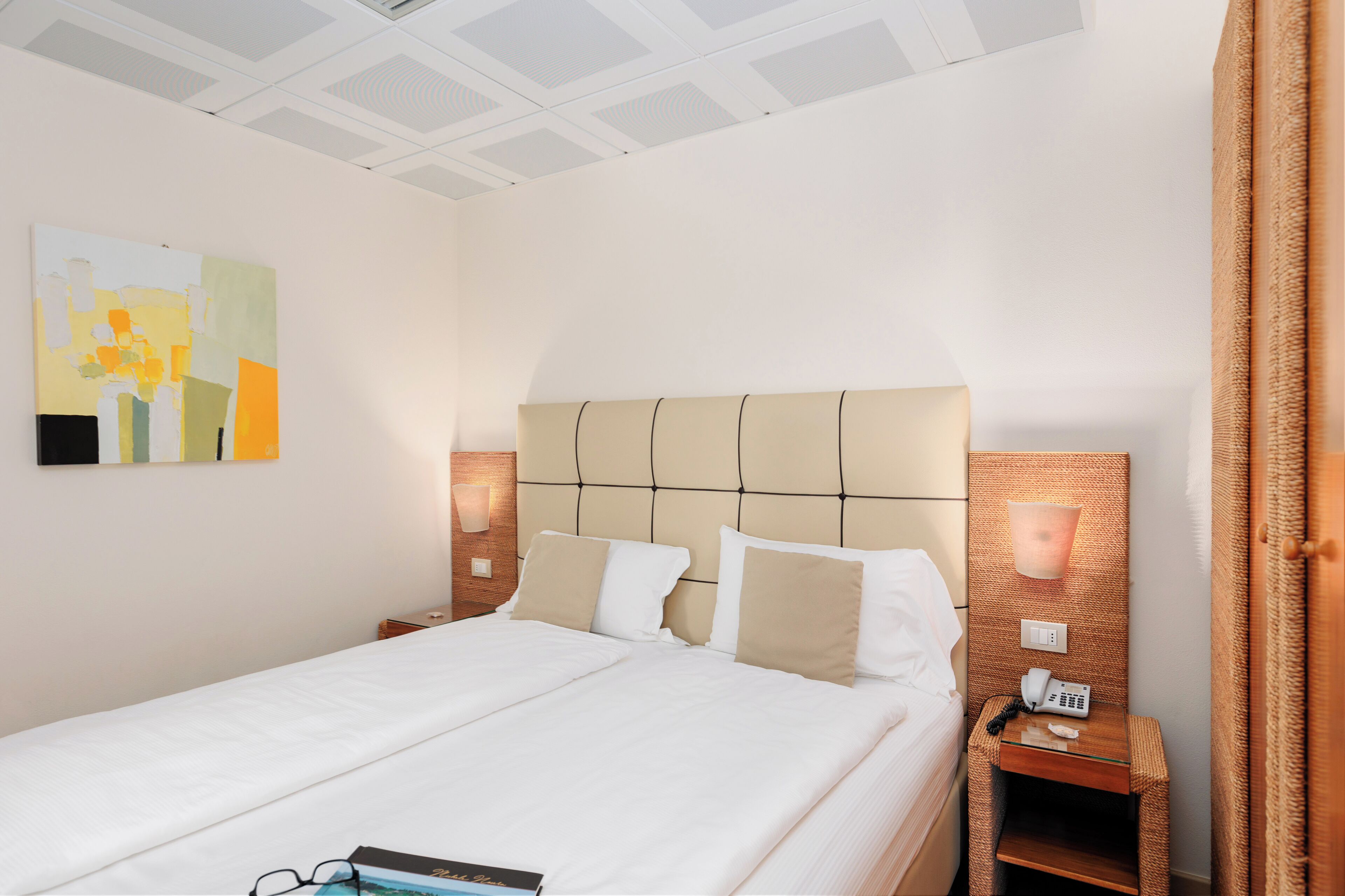 Een hotelkamer met een groot bed, een nachtkastje met een telefoon en een wandlamp.