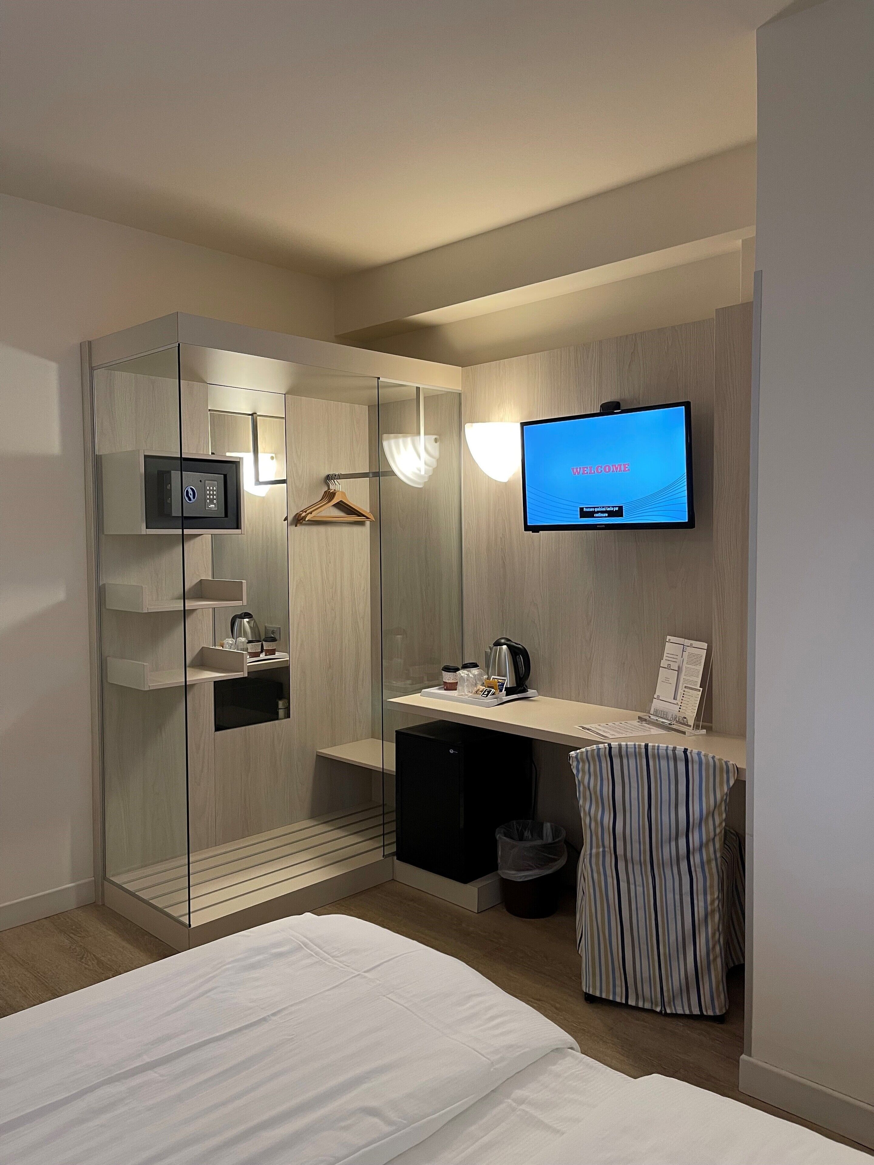 A modern hotel room with a bed, a desk with a computer, a television, and a minibar.