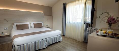 A hotel room with a large bed, bedside tables, a desk with breakfast items, and a window with curtains.