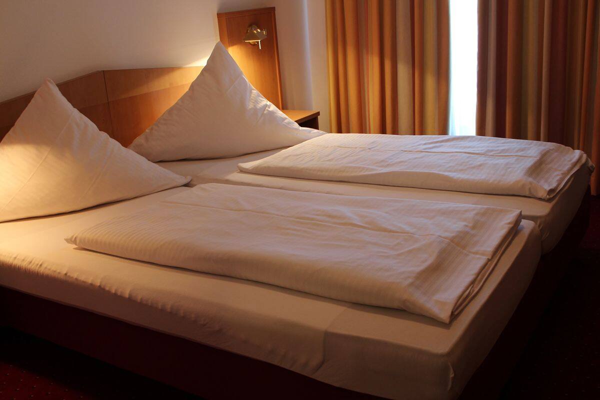 Un lit double avec du linge de lit blanc et des oreillers, une tête de lit en bois et une table de chevet avec une lampe.