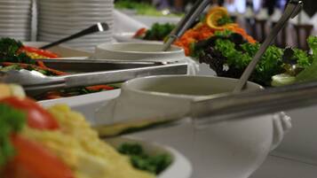 Buffet com diversos pratos, incluindo saladas e legumes, dispostos em pratos brancos e talheres.