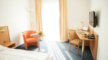 Een hotelkamer met een bed, een bureau, twee stoelen, een televisie en een raam met gordijnen.
