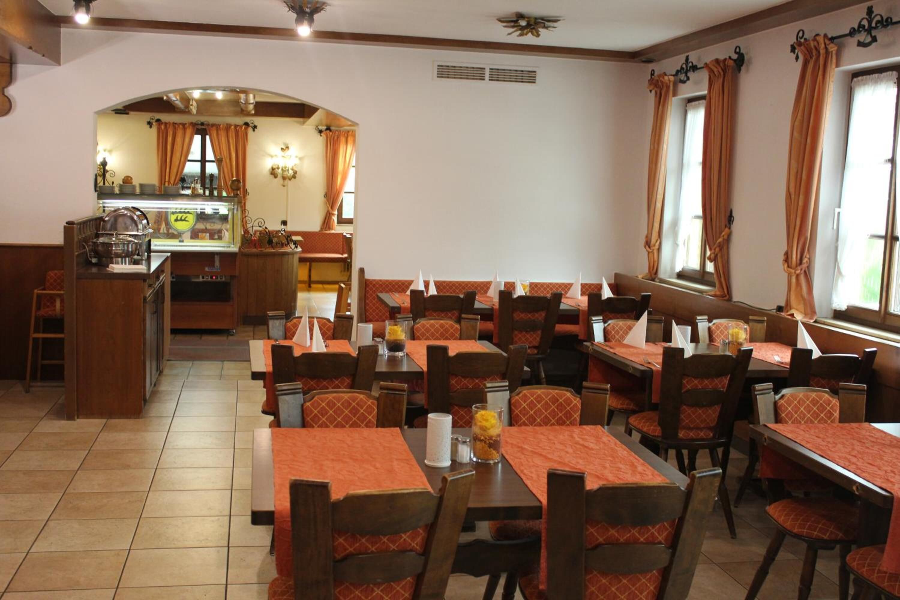 A restaurant with multiple tables and booths, a kitchen area, and a seating area with orange curtains.
