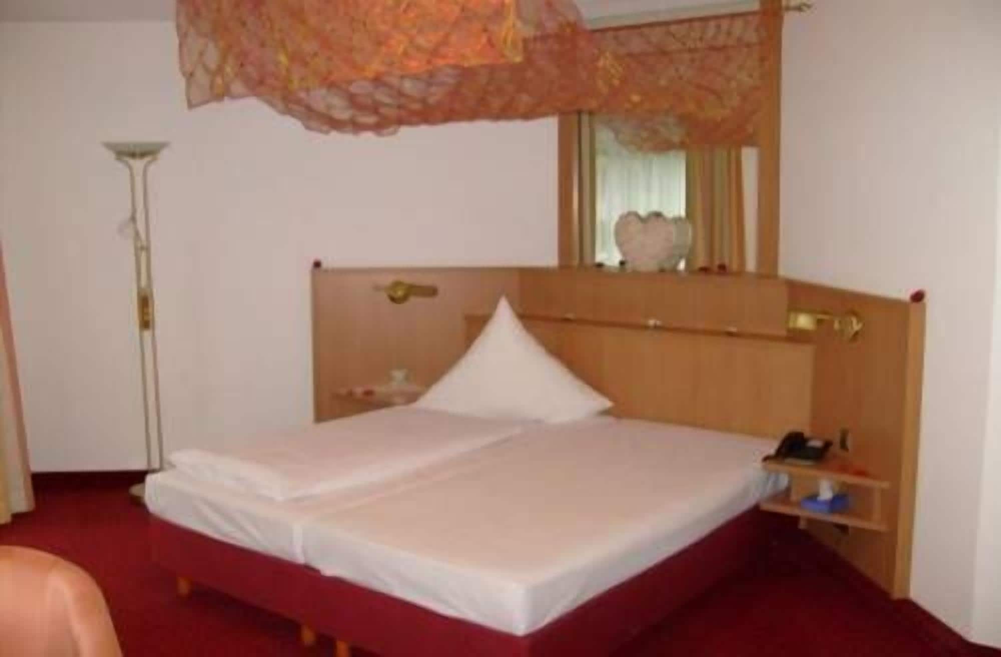 Habitación de hotel con una cama de madera, una mesita de noche, una lámpara y un espejo en la pared.