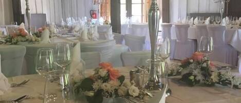 A banquet hall with tables set for a formal event, featuring floral centerpieces and elegant tableware.