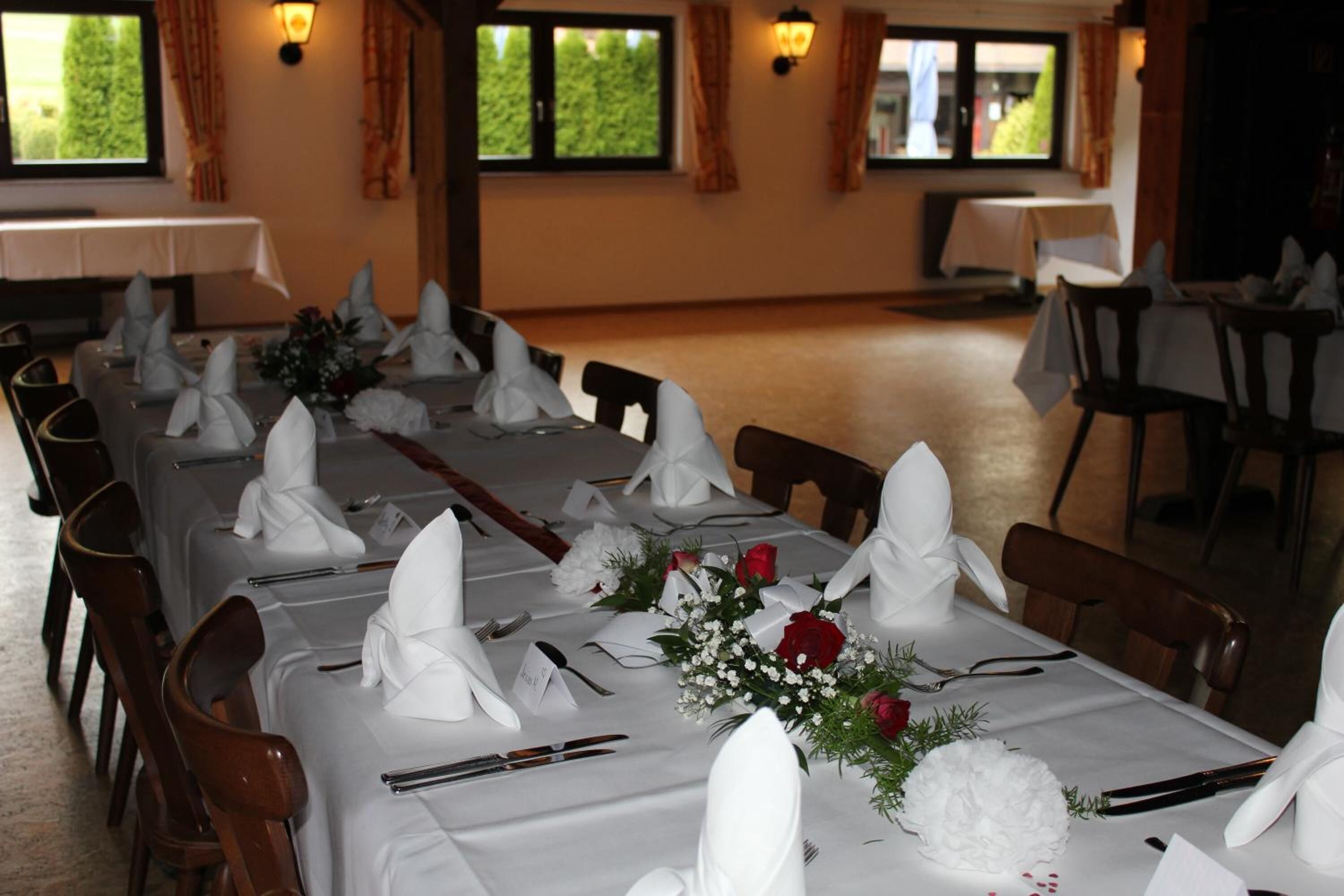 A dining area with tables set for a meal, featuring white tablecloths, folded napkins, and floral centerpieces.