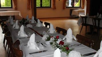 A dining area with tables set for a meal, featuring white tablecloths, folded napkins, and floral centerpieces.