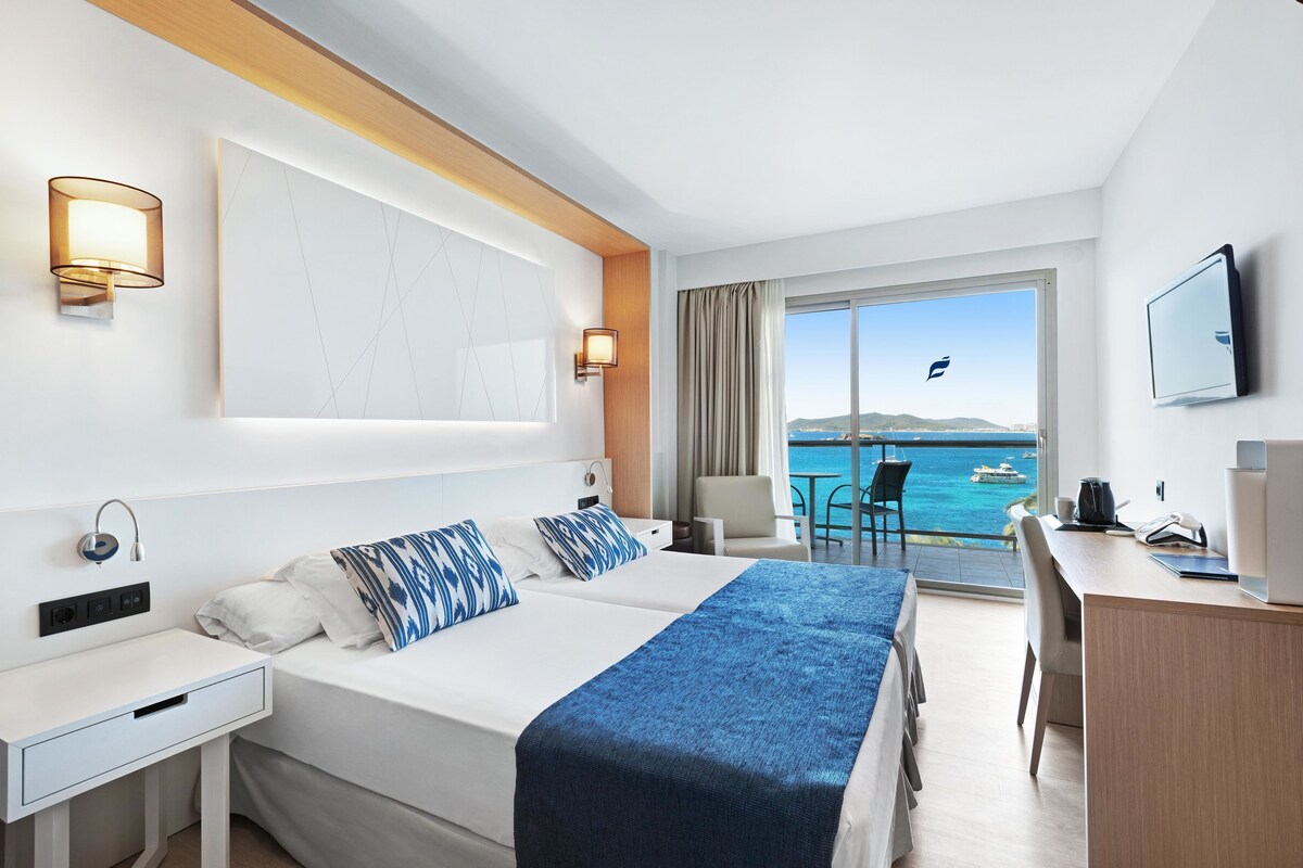 Una habitación de hotel con cama, escritorio y vista al mar.