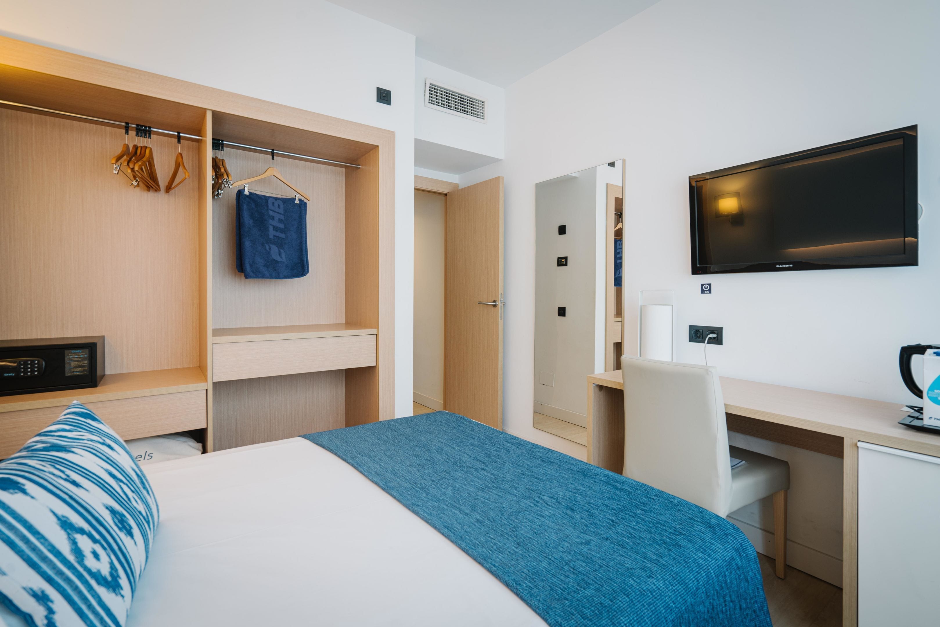 A hotel room with a bed, a desk, a TV, a wardrobe, and a hanging coat rack.