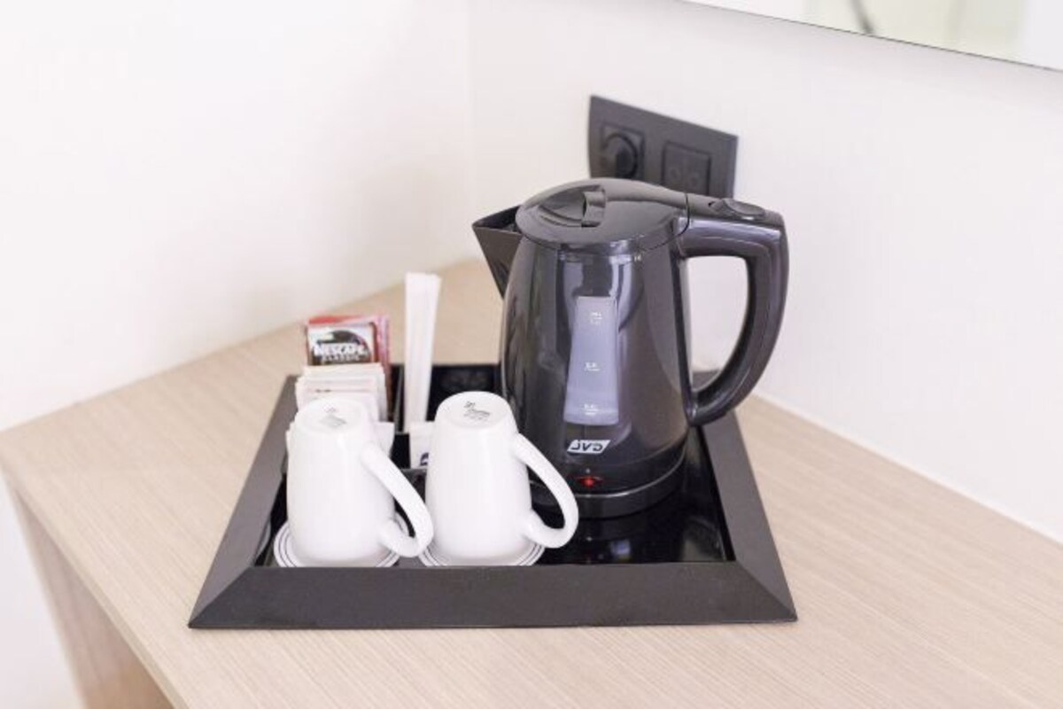 Una cafetera negra con pantalla digital, dos tazas blancas y una caja de café instantáneo sobre una mesa de madera.