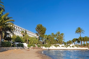 Un hotel frente a la playa con piscina, palmeras y un cielo azul despejado.